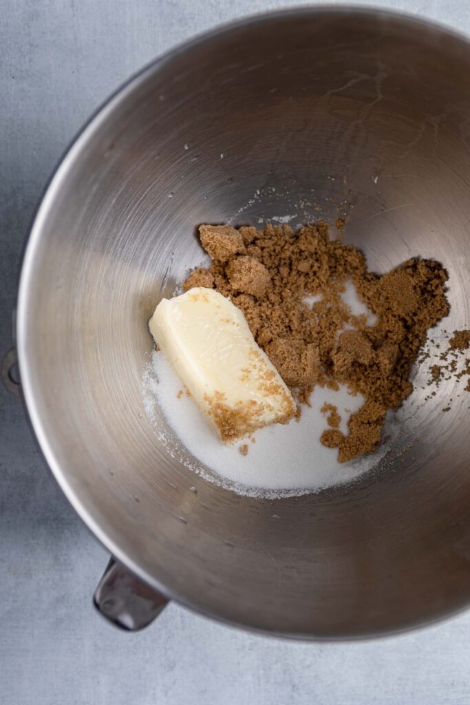 stick of butter with brown and white sugar in a metal mixing bowl 