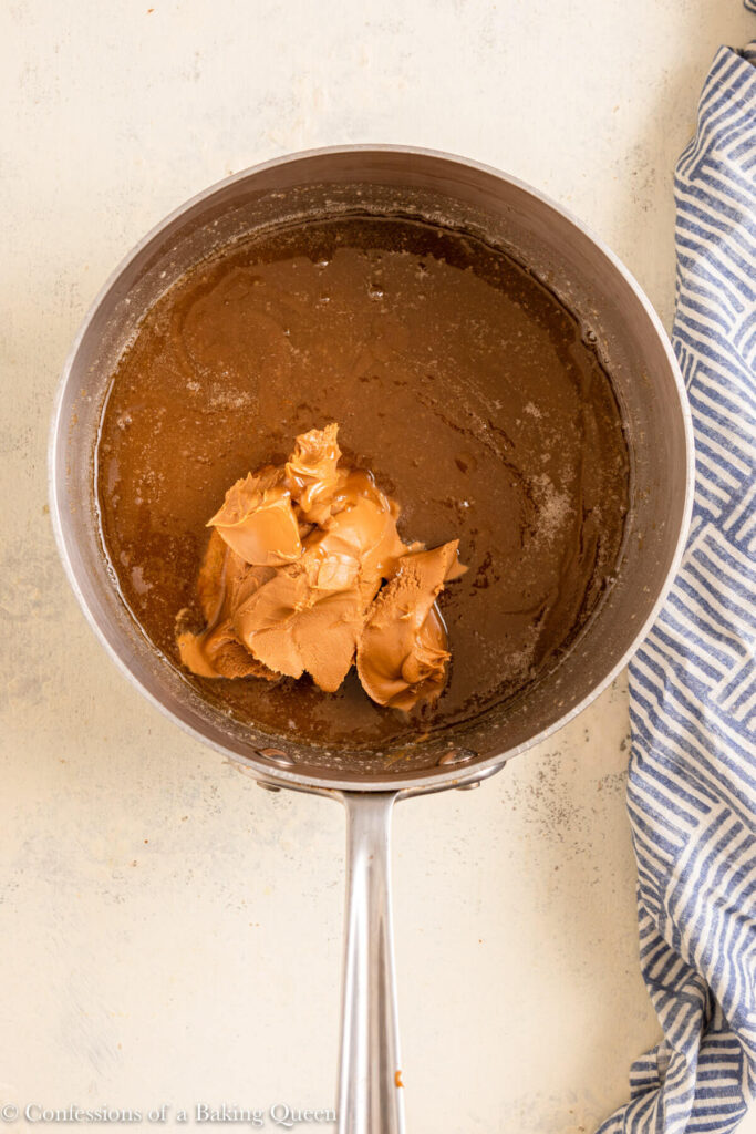 cookie butter added to melted butter and sugar in a metal pot on a white surface with a blue linen