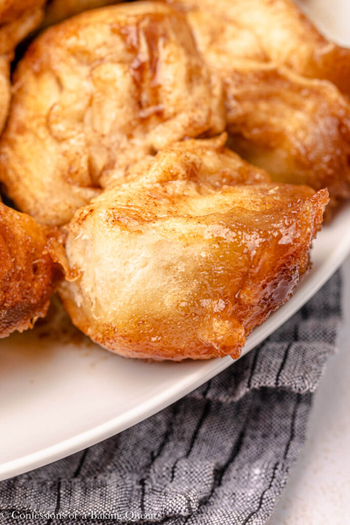 close up of a piece of monkey bread pulled apart on a white plate on a blue linen