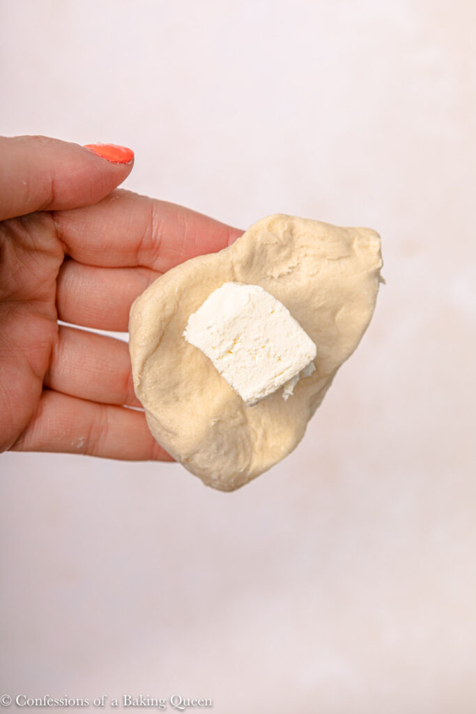 cream cheese cube added to biscuit dough hand holding it over a light pink surface