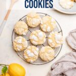 lemon crinkle cookies cooling on a wire rack next to a plate of cookies, lemons, dishtowel and a wooden spoon