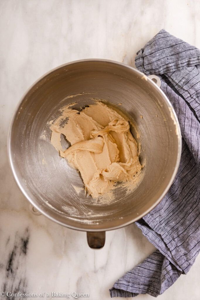 creamed butter and sugar in a metal mixing bowl on a marble surface with a blue stripped linen