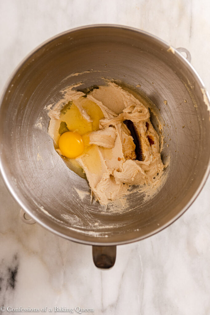 egg and vanilla extract added to butter mixture in a metal bowl on a marble surface
