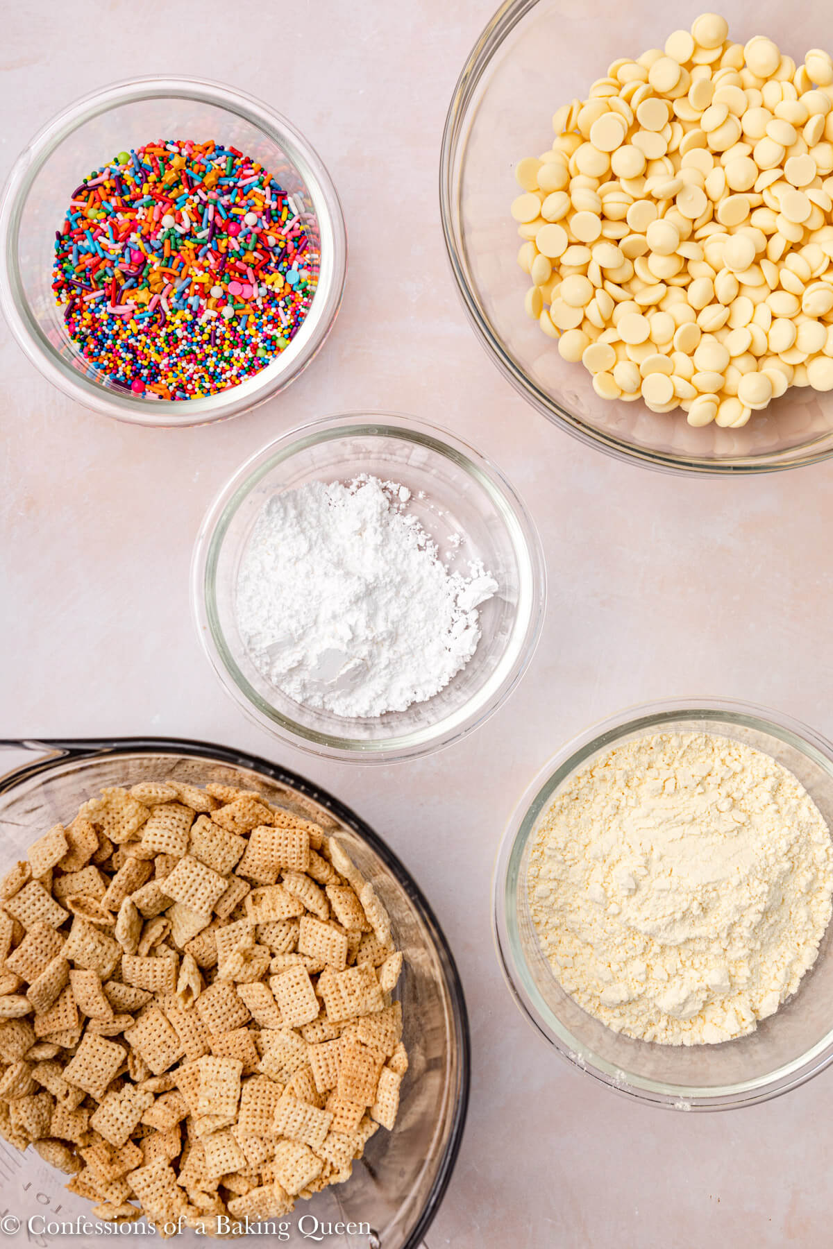 ingredients for cake batter puppy chow in individual bowls on a light pink surface