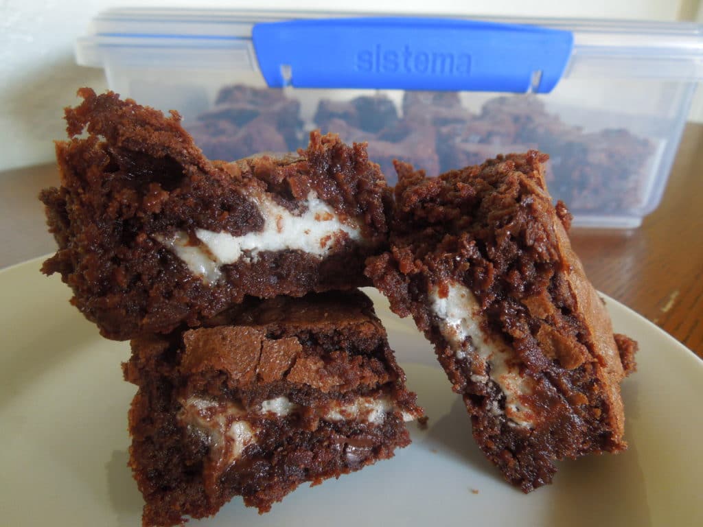 three Peppermint Patty Stuffed Brownies on a white plate on a wood table with a container of more brownies in the background