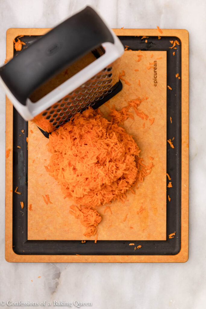 carrots finely shredded with a box grater on a wood cutting board on a white marble surface
