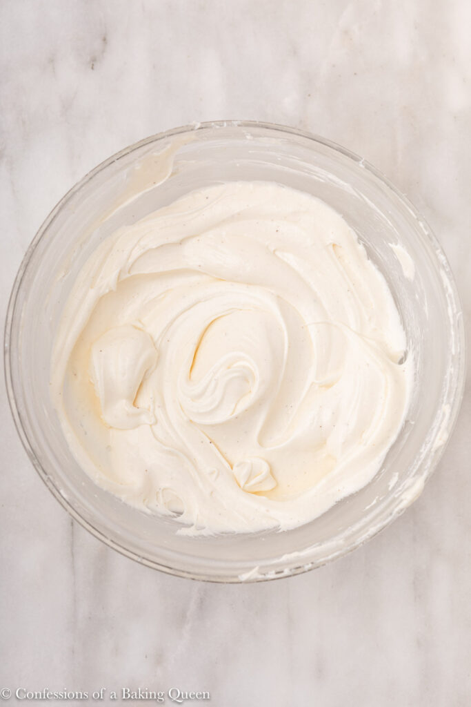 cream cheese frosting in a glass bowl on a white marble surface