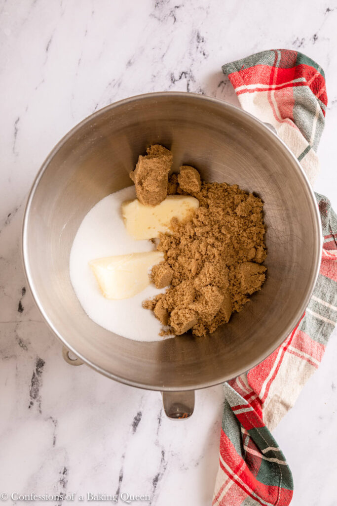brown sugar, granulated sugar and butter in a metal mixing bowl on a marble surface with a Christmas linen