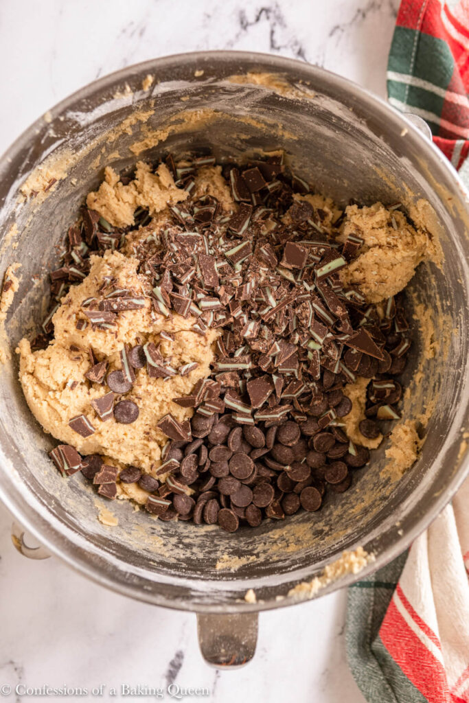 chopped andes and chocolate chips added to cooke dough in a metal bowl on a marble surface with a Christmas linen