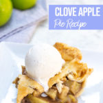 clove apple pie slice with a scoop of vanilla ice cream on top on a white square plate with a green apple in the background