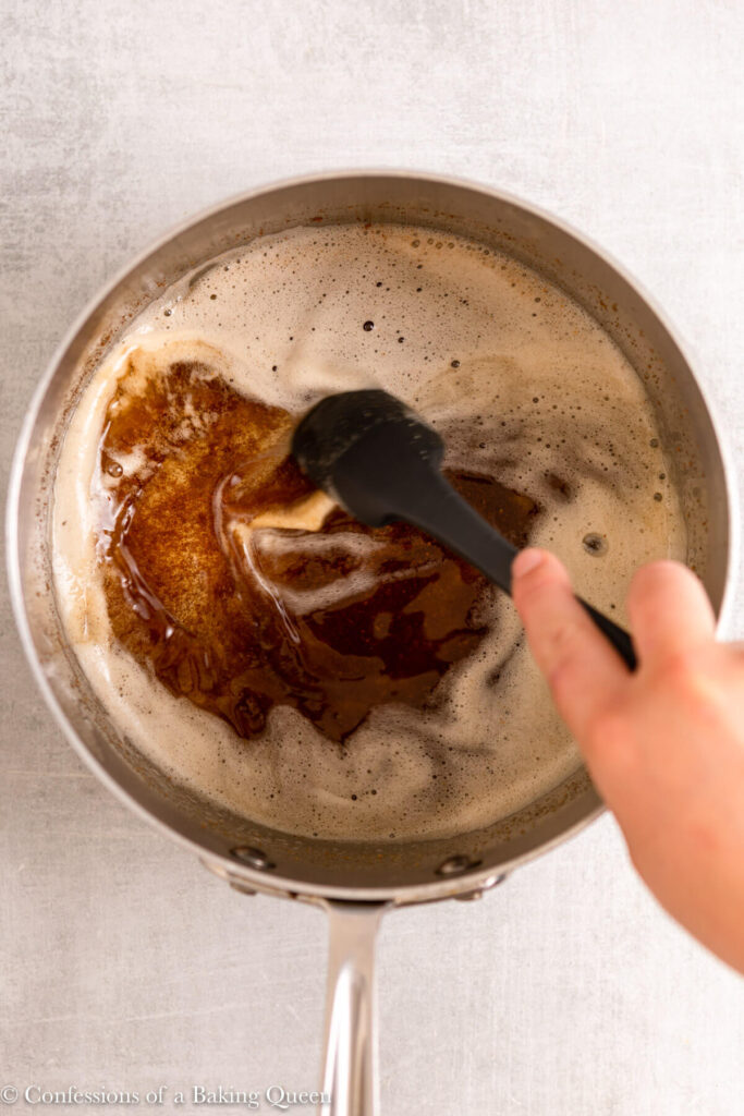 butter browning in a metal pan with a spatula swirling it around on a light grey surface