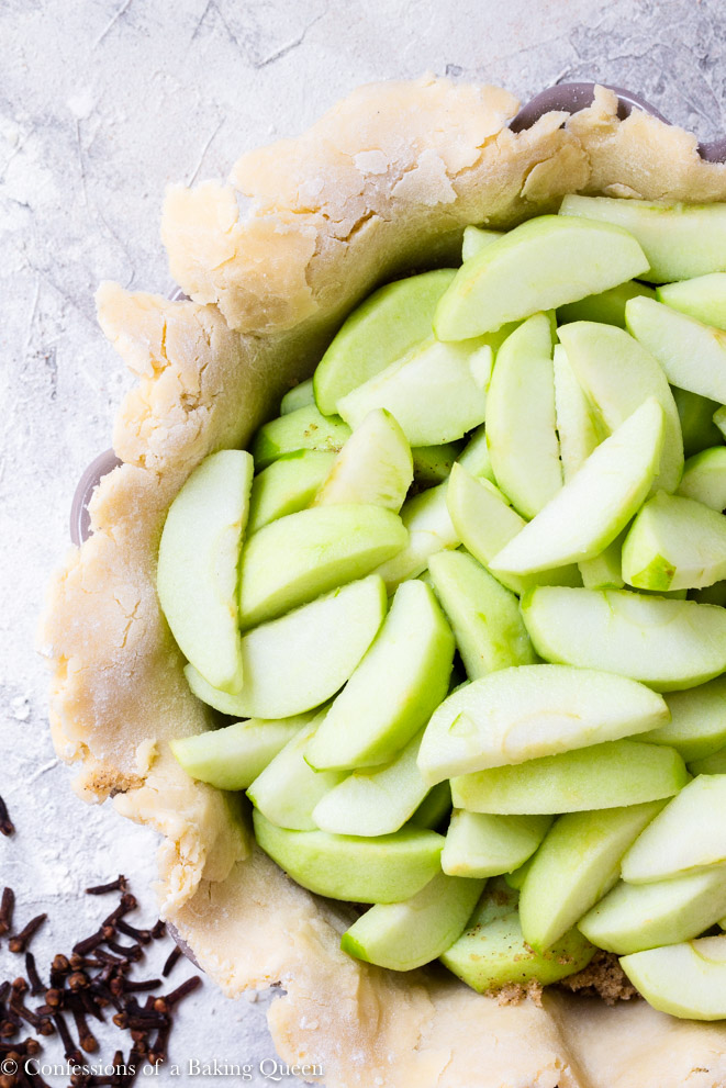 apples slices inside a pie crust on a grey surface with some cloves