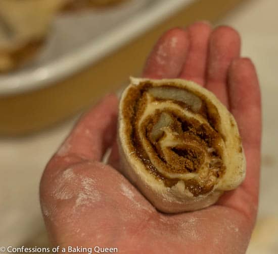 Salted Caramel Apple Cinnamon Roll cut into an individual roll showing the swirls held in a hand over a kitchen counter background