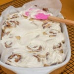 Salted Caramel Apple Cinnamon Rolls frosted with a pink spatula sitting on a wire rack on a wood table