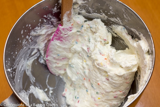 pink spatula mixing golden oreo cake batter ice cream mixture in a metal bowl on a wood table