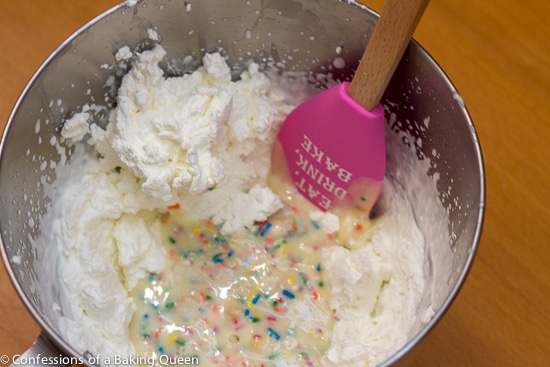 Cake Batter Golden Oreo Ice Cream being made the toppings being mixed into cream mixture with a pink spatula in a silver bowl on a wood table