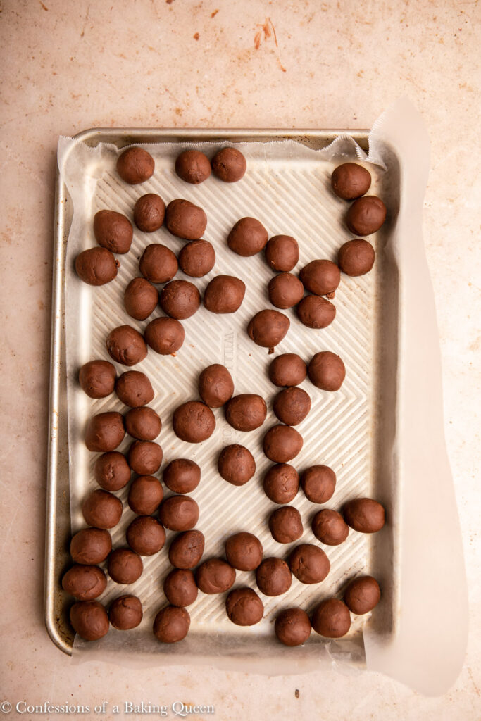 chocolate truffle balls on a wax lined baking sheet on a light brown surface
