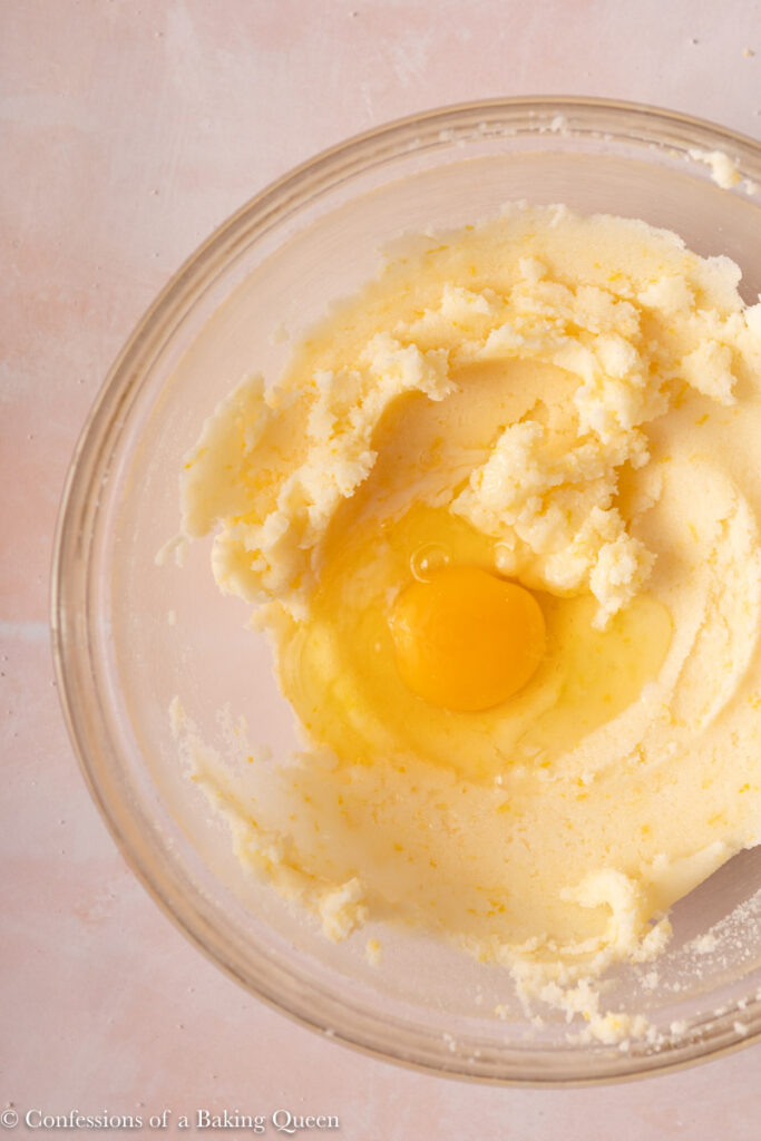 egg added to creamed butter and sugar in a glass bowl on a light pink surface
