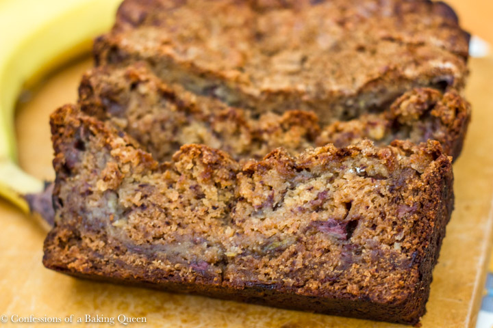 close up of pudding banana bread slice on wood board with a banana in the background