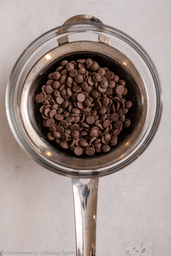 chocolate chips in a glass bowl over a double boiler on a light grey surface