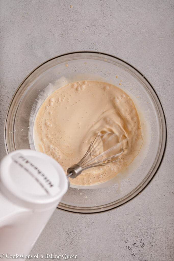electric mixer whisking heavy cream and baileys together in a glass bowl on a light grey surface