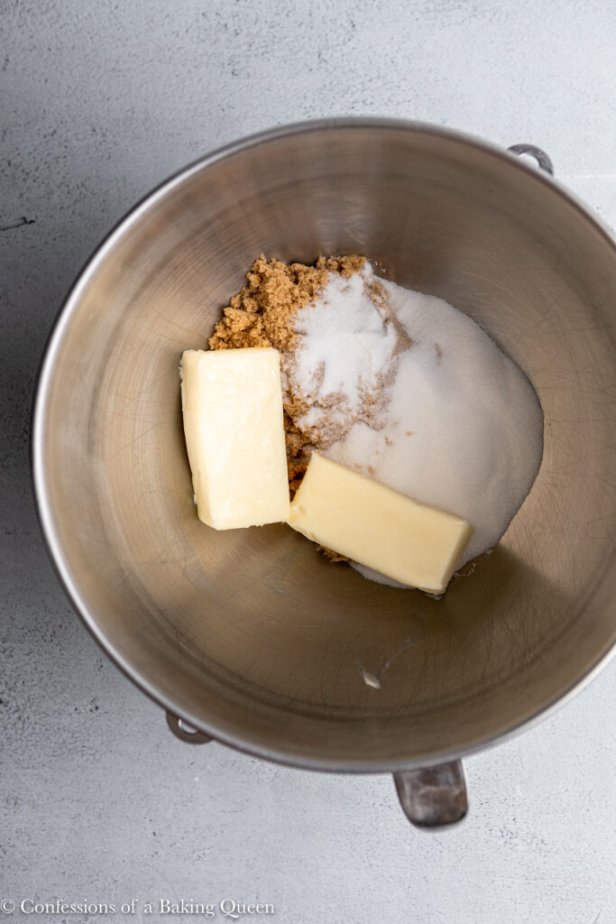 metal mixing bowl with brown sugar, white sugar, and butter in on a grey surface