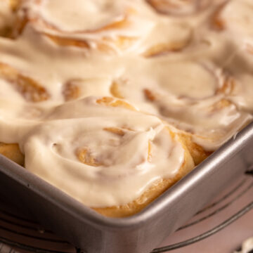 cream cheese frosted cinnamon rolls in a pan next to a knife and linen