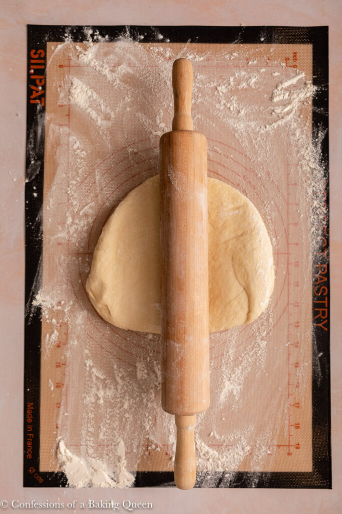dough with a rolling pin on top on a floured work surface on a light pink surface