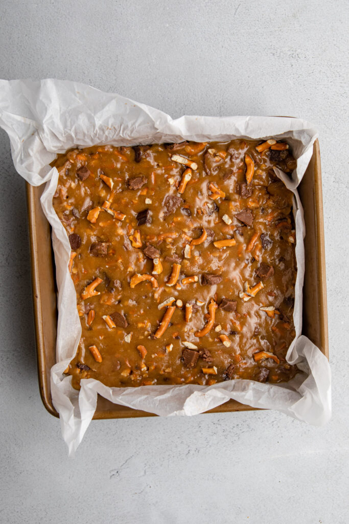 pretzel chocolate chunk blondies in a parchment paper lined pan on a grey surface