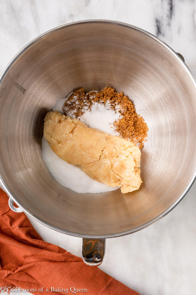brown butter and sugars in a metal mixing bowl on a white marble surface with an orange linen