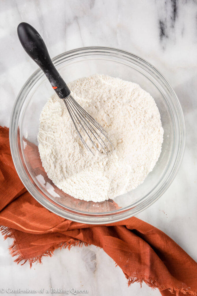 dry ingredients whisked together in a glass bowl on a white marble surface with an orange linen