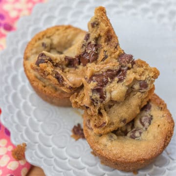 Biscoff Stuffed Chocolate Chip Cookies broken in half stacked on top of each other on a purple plate with a pink napkin on a wood board