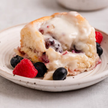 berry sweet roll served on a white plate with a few more berries on a light grey surface