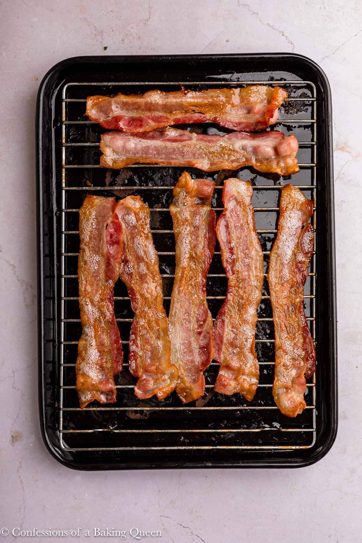 bacon cooked on a wire rack on top of a black tray on a light surface.