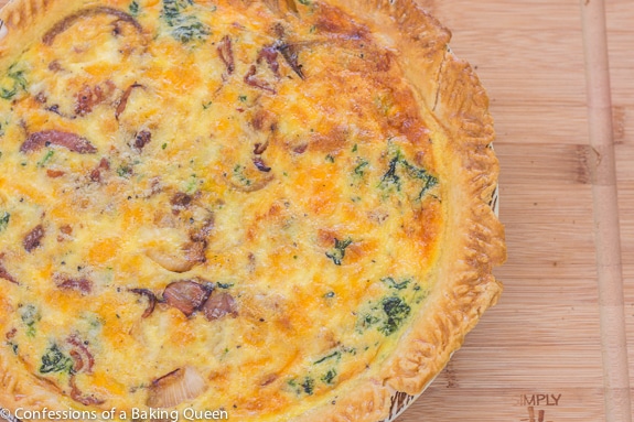 Bacon, Onion, Spinach Quiche baked in a pie dish on a wood board 