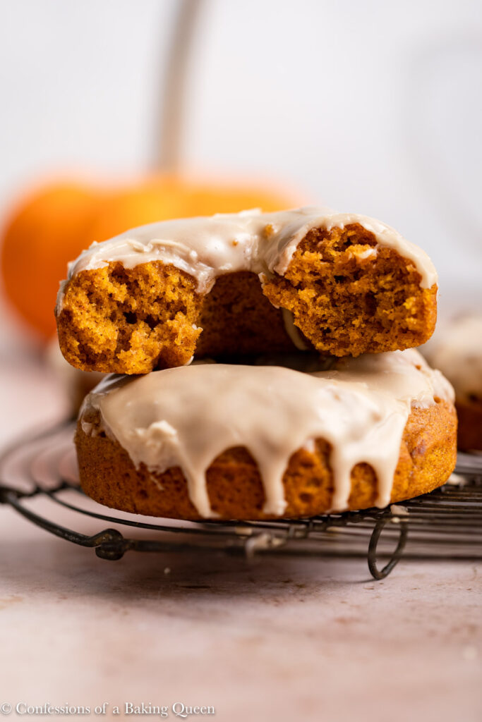 maple glazed pumpkin donuts on wire rack with a pumpkin in the background