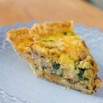 Bacon, Onion, Spinach Quiche slice on a purple plate on a wood board