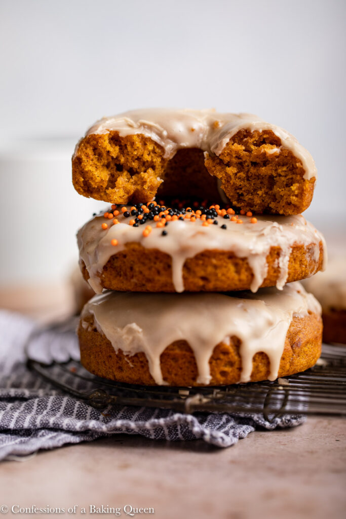 stack of pumpkin cake donuts  on a black cooling rack on top of a blue striped towel