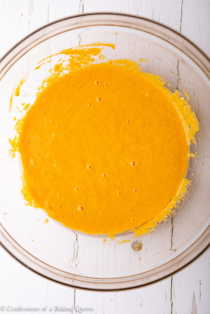wet ingredients for pumpkin bread mixed together in a glass bowl on a white wood surface