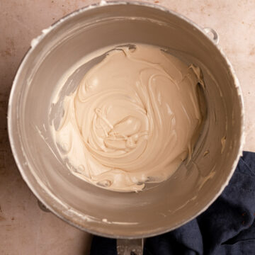 maple cream cheese frosting in a metal bowl on a light brown surface with a blue linen