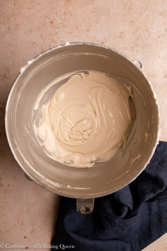 maple cream cheese frosting in a metal bowl on a light brown surface with a blue linen