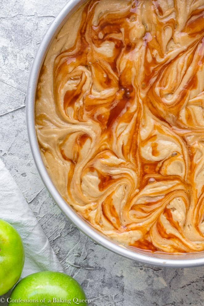 salted caramel swirled into cake batter for an upside down caramel apple cake recipe on a grey surface with a white linen and two granny smith apples