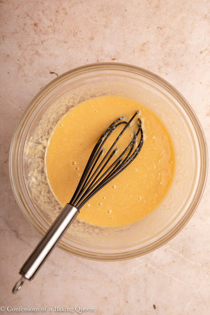 wet ingredients whisked together in a bowl with a metal and black whisk on a light brown surface