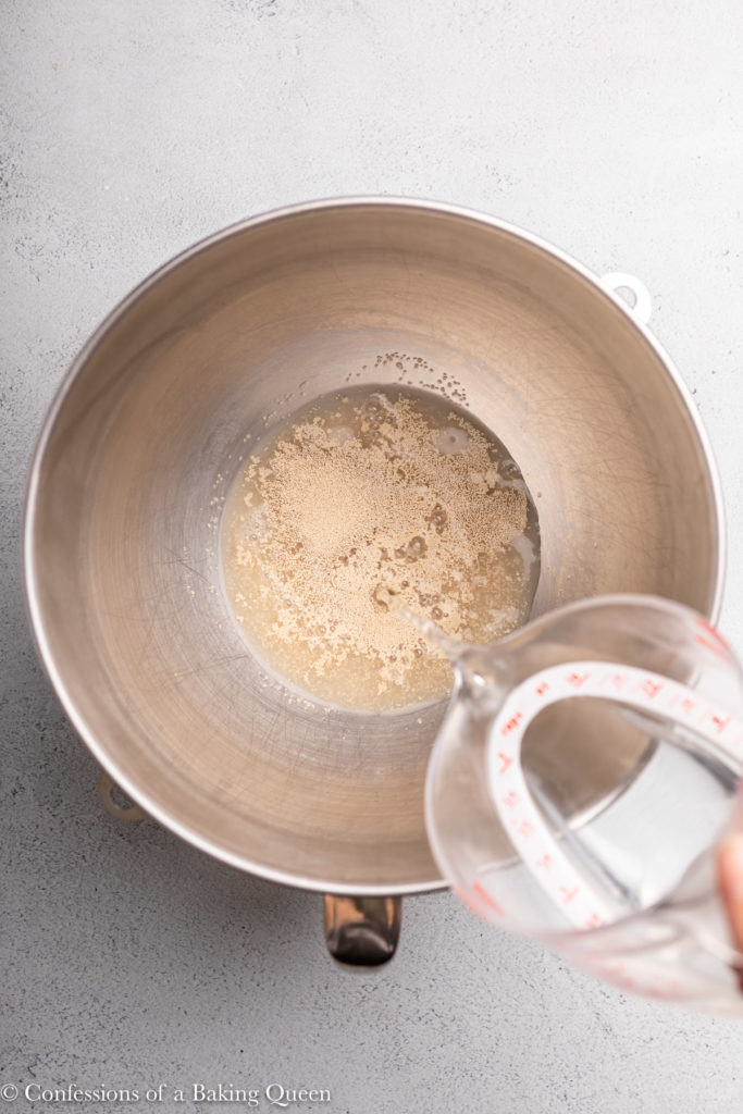 water being poured into a metal bowl with yeast in