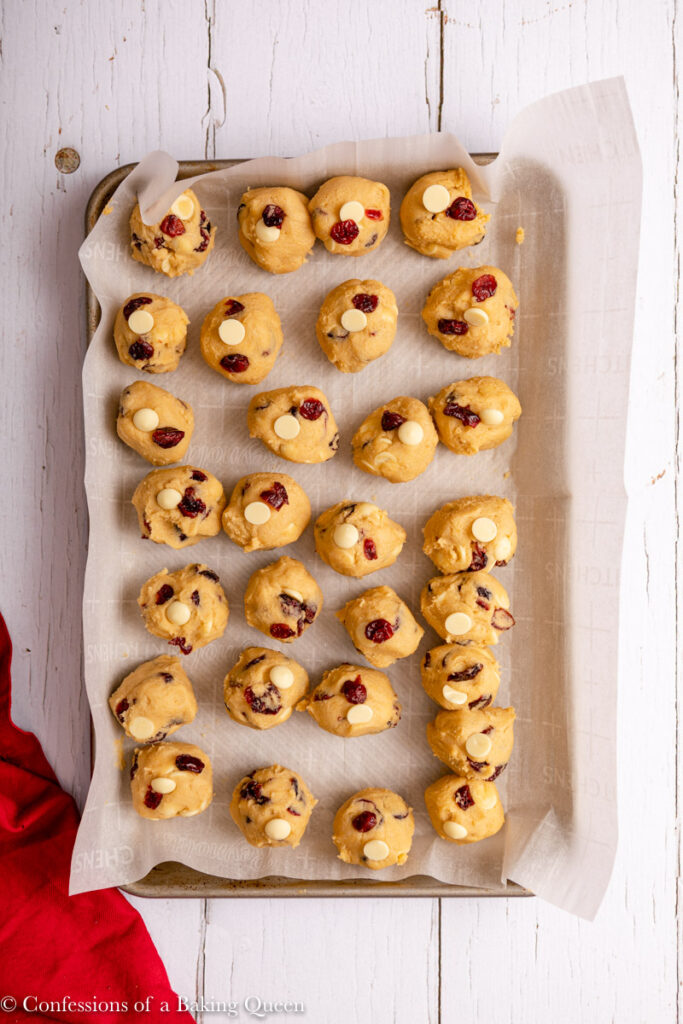 white chocolate cranberry cookie dough balls on a parchment lined baking sheet on a white wood surface with a red linen