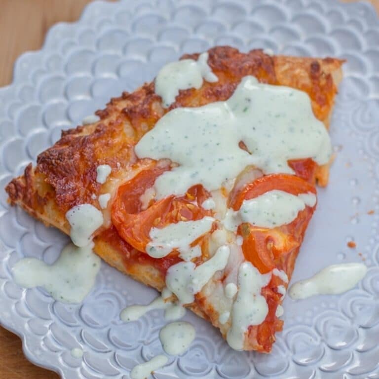 Homemade ranch dressing drizzled on a slice of pizza on a pink plate on a wood board