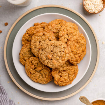 cookie butter oatmeal butterscotch cookies on a plate next to a glass of milk and small cup of oats