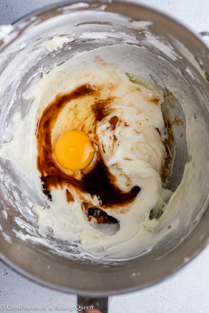 egg and vanilla extract added to cream cheese mixutre in a metal bowl on a grey surface