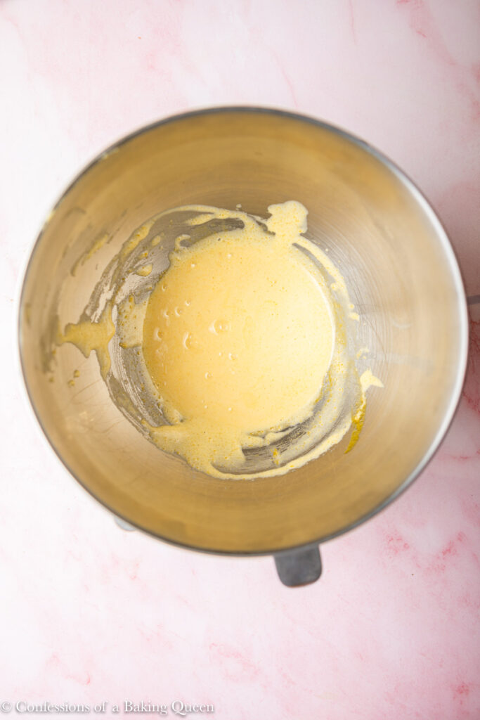 lightened whisked egg yolk mixture in a metal bowl on a light pink surface