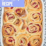 Homemade Strawberry Sweet Rolls baked to golden brown in a white ceramic dish on a wire rack on a white wood background